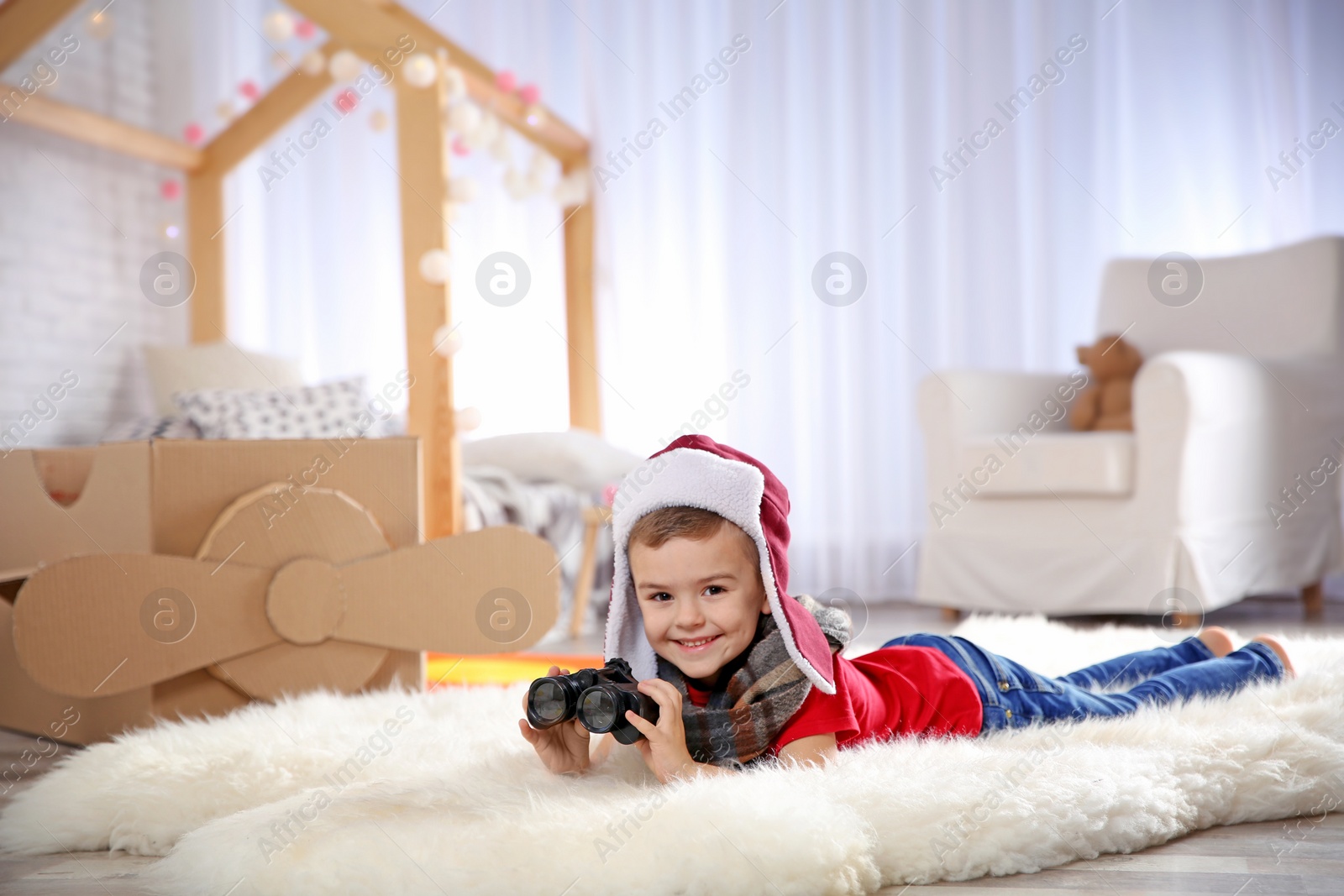 Photo of Cute little boy playing with binoculars and cardboard airplane in bedroom