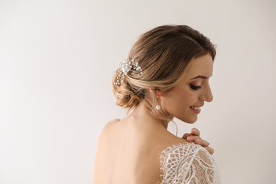 Young bride with elegant wedding hairstyle on light background