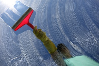 Woman cleaning glass with squeegee on sunny day