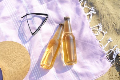 Photo of Bottles of beer and beach accessories on sand, flat lay
