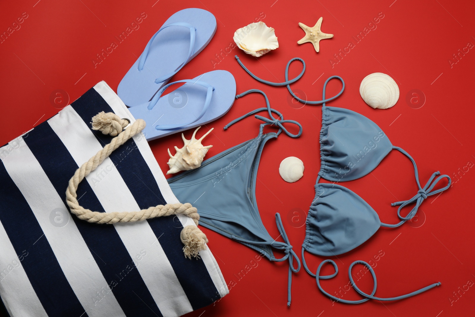 Photo of Stylish bag with beach accessories on red background, flat lay