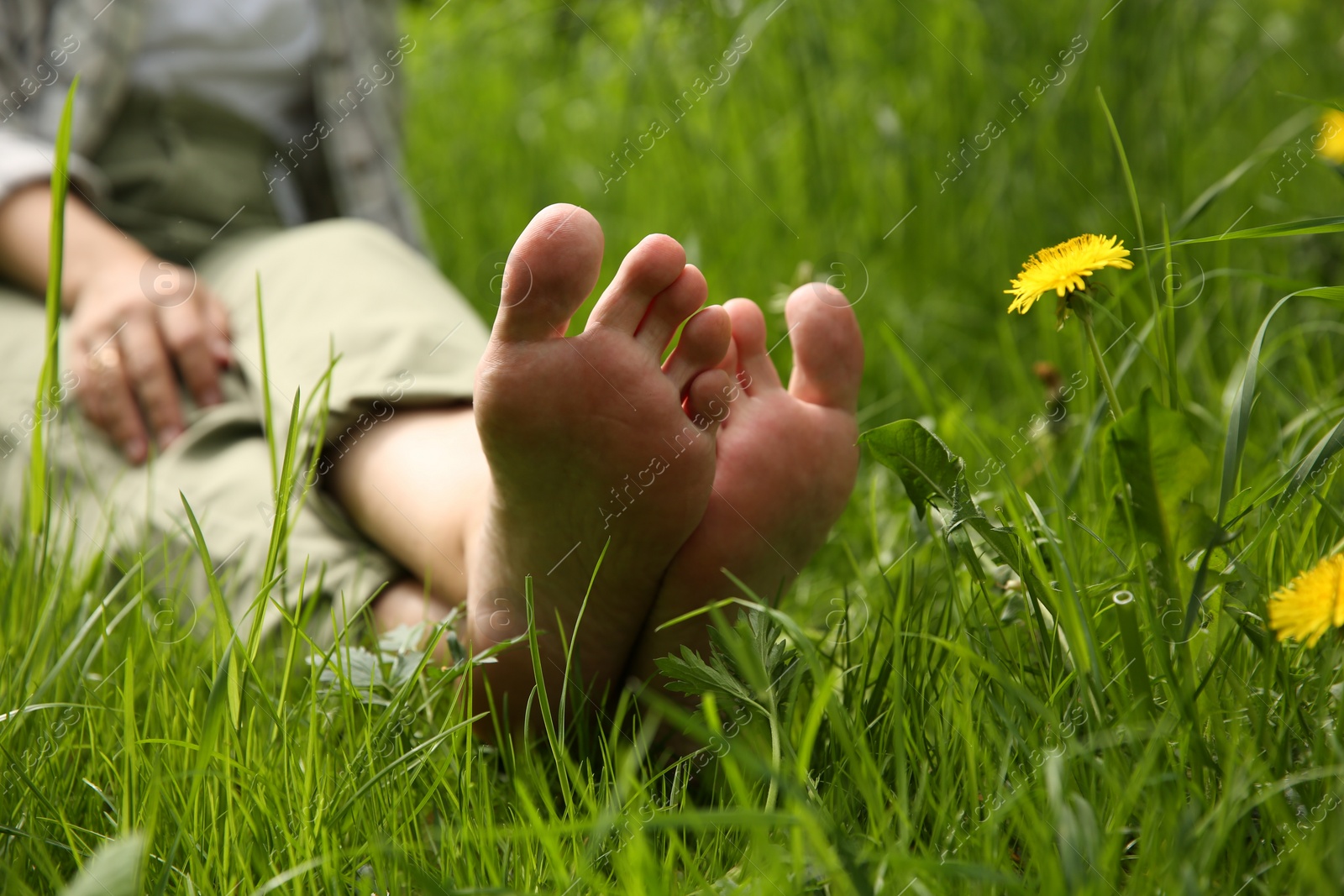 Photo of Woman sitting barefoot on green grass outdoors, closeup