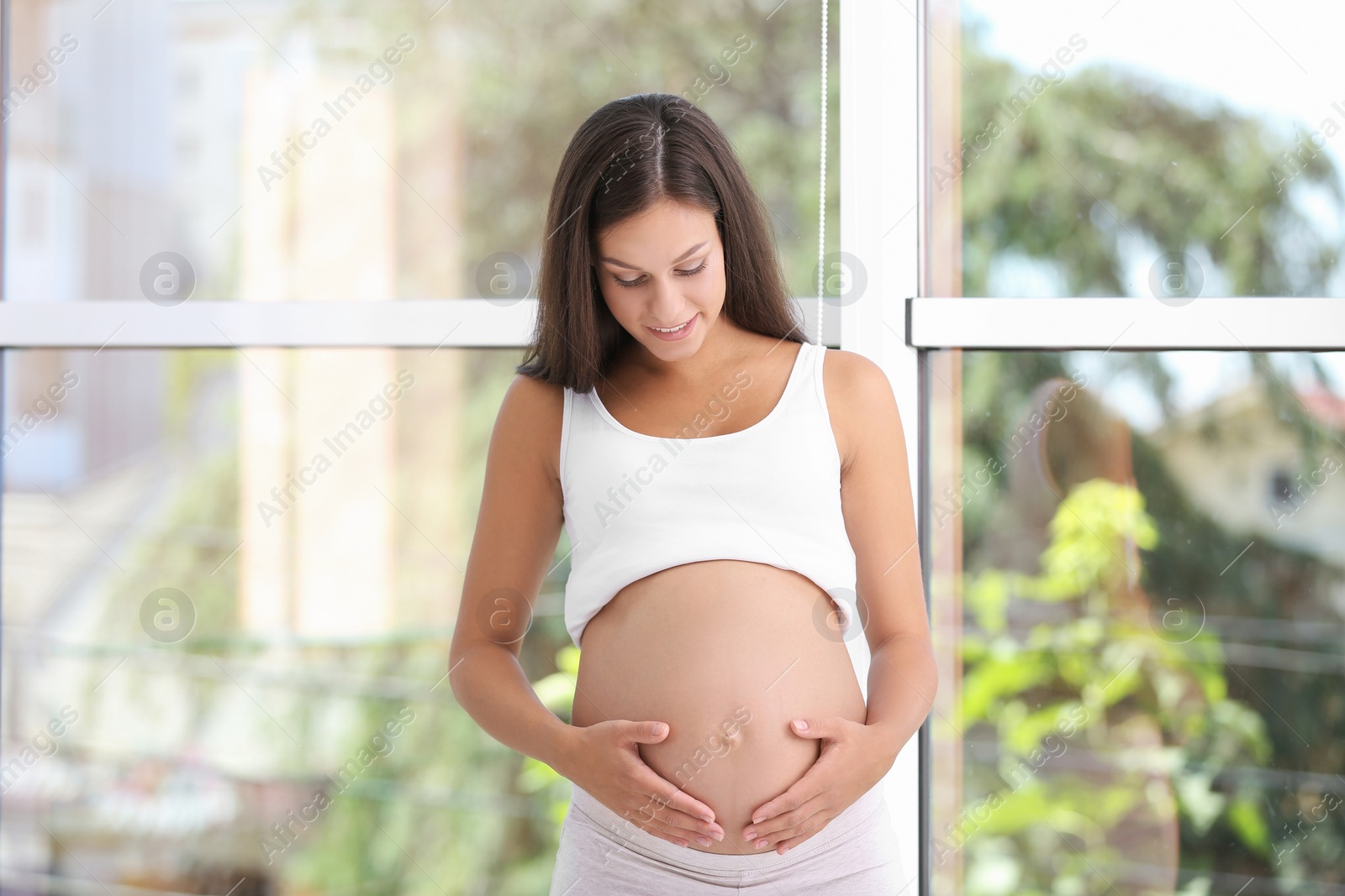 Photo of Happy pregnant woman standing near window at home