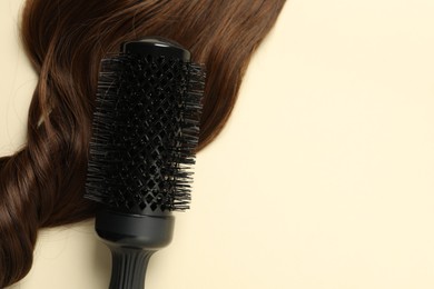 Professional round brush with brown hair strand on beige background, top view. Space for text