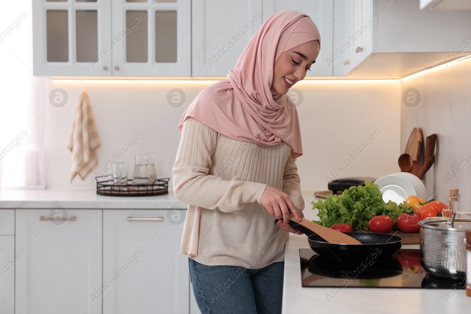 Photo of Muslim woman cooking delicious dish with vegetables on cooktop in kitchen