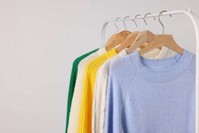 Photo of Rack with different warm sweaters on light background. Space for text