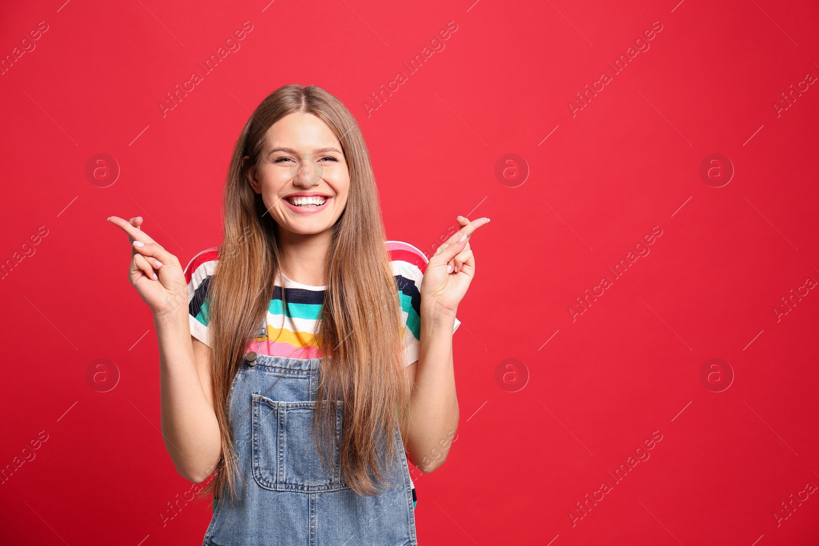 Photo of Portrait of hopeful woman with crossed fingers on red background