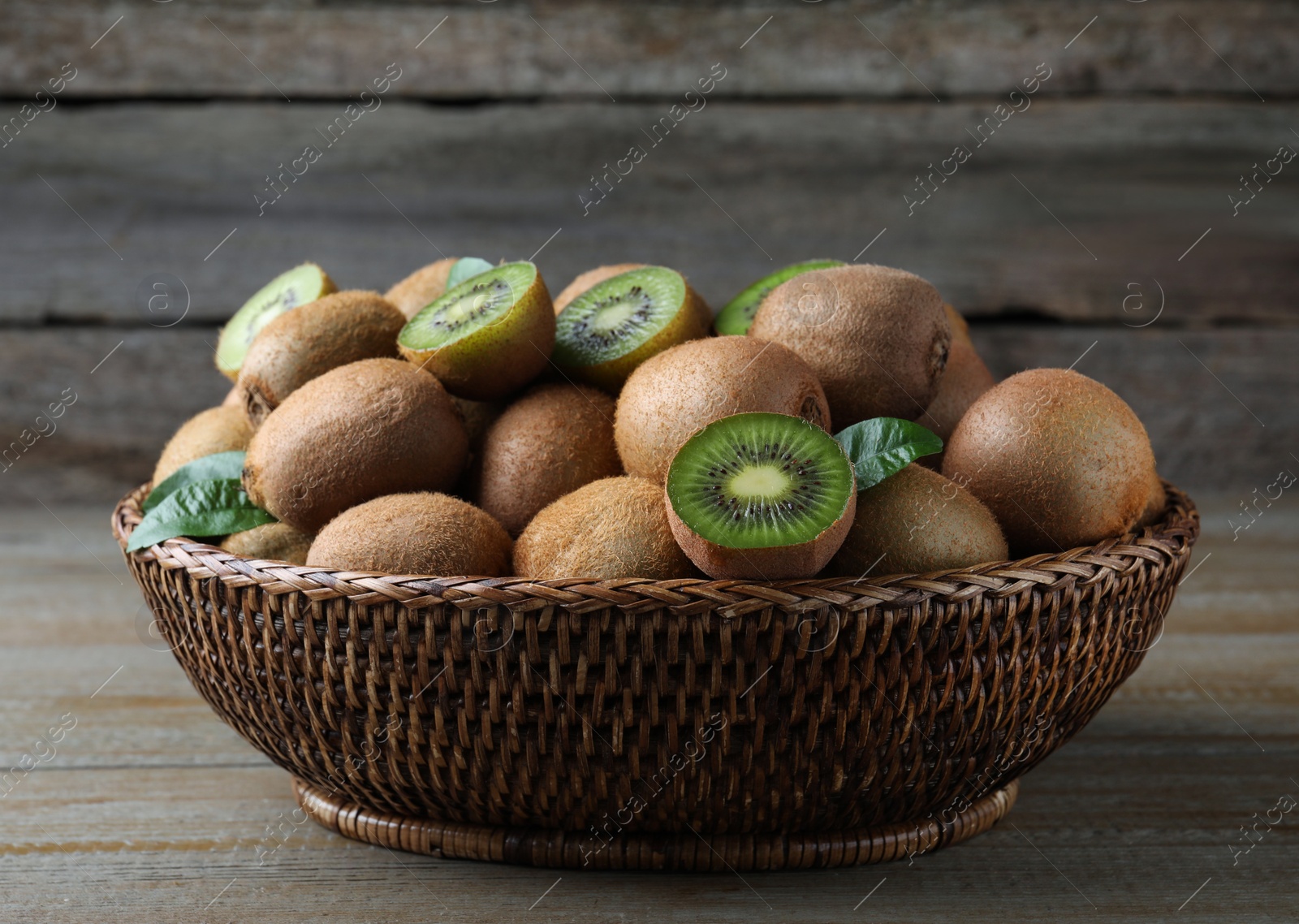Photo of Fresh ripe kiwis in wicker bowl on wooden table