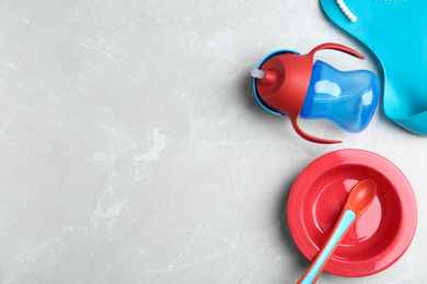 Set of colorful plastic dishware on light grey marble table, flat lay with space for text. Serving baby food