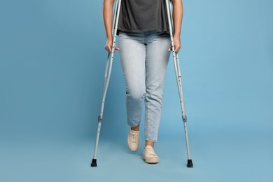Woman with crutches on light blue background, closeup