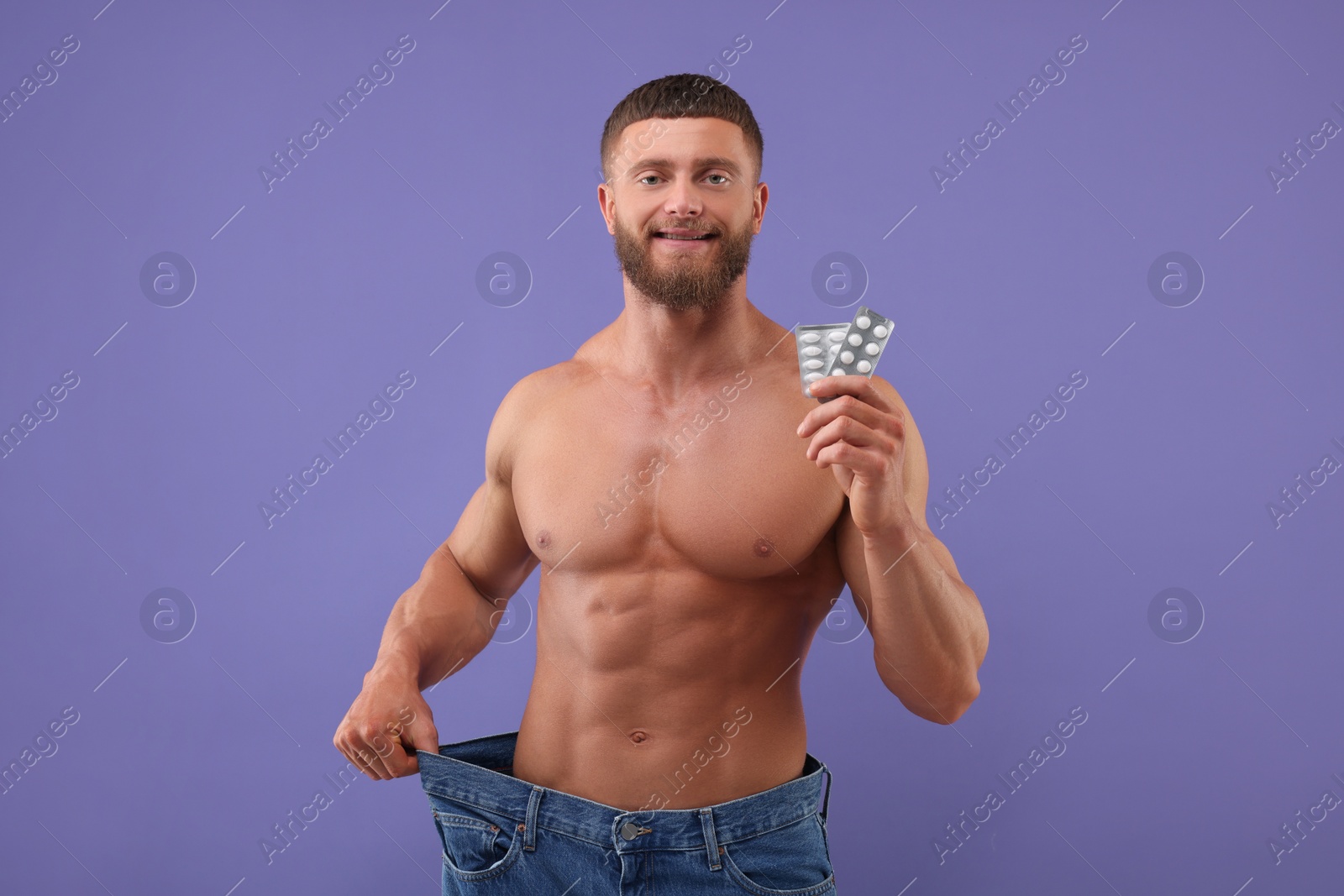 Photo of Athletic young man with pills wearing big jeans on purple background. Weight loss