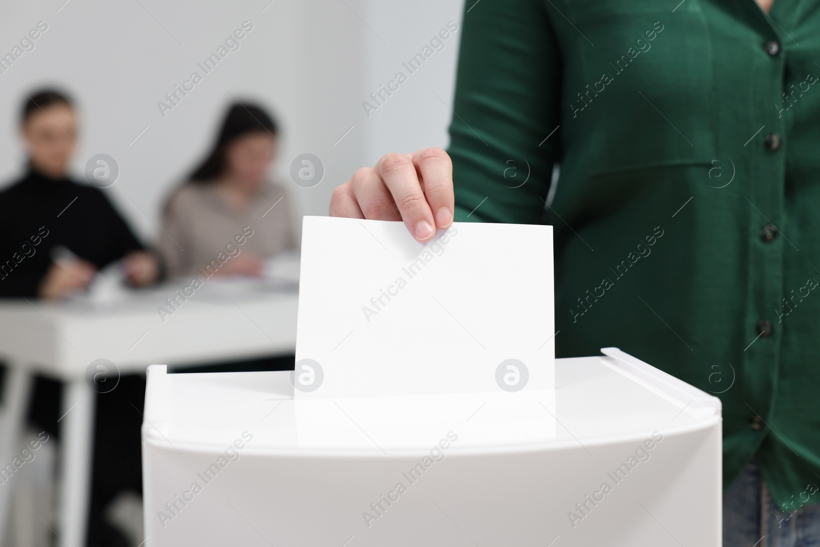 Photo of Woman putting her vote into ballot box on blurred background, closeup