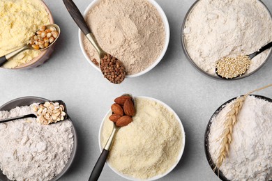 Photo of Bowls with different types of flour and ingredients on light grey table, flat lay