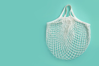 Photo of Empty white net bag on turquoise background, top view. Space for text