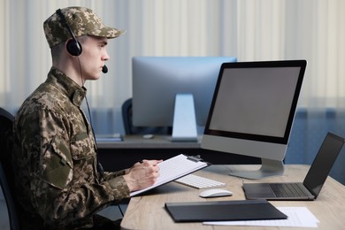 Photo of Military service. Young soldier with clipboard and headphones working at table in office
