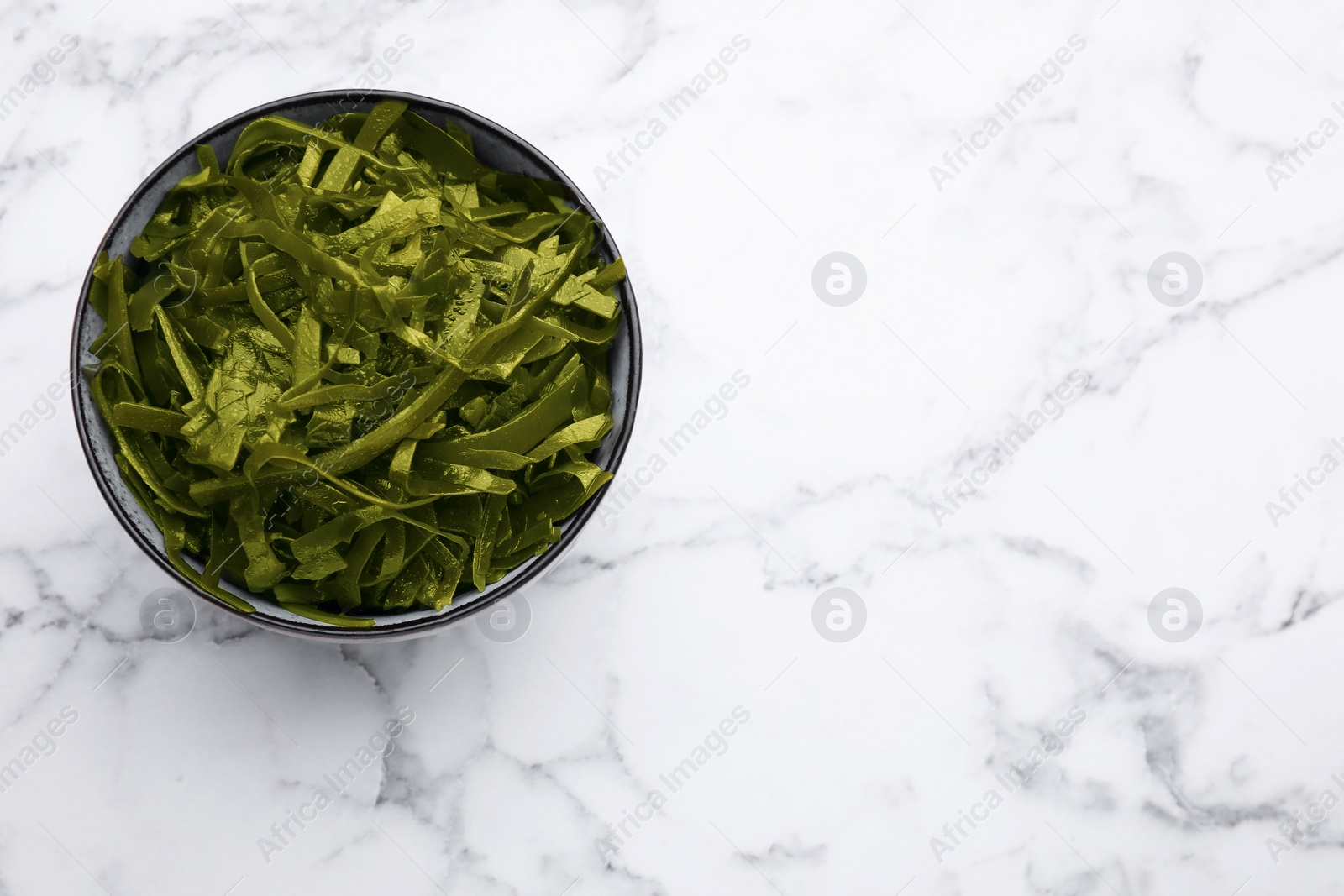 Photo of Fresh laminaria (kelp) seaweed in bowl on white marble table, top view. Space for text