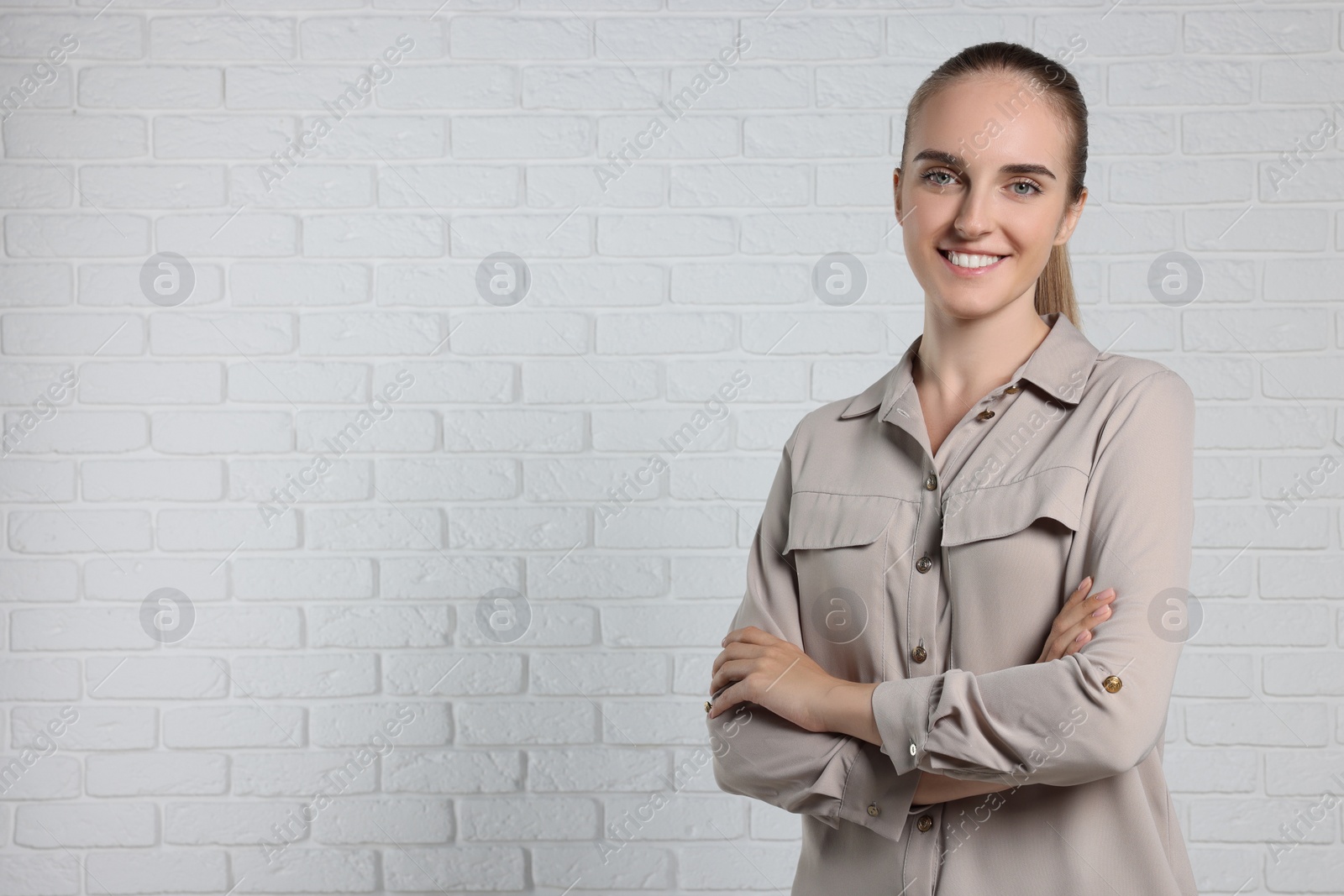 Photo of Happy young secretary with crossed arms near white brick wall, space for text