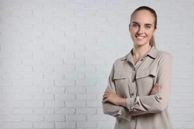 Photo of Happy young secretary with crossed arms near white brick wall, space for text