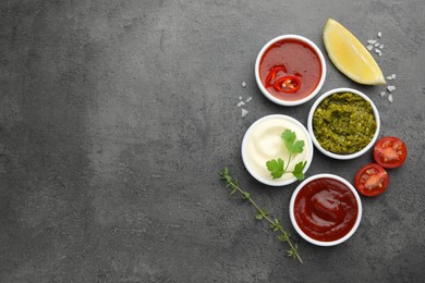 Different tasty sauces in bowls and ingredients on grey table, flat lay. Space for text