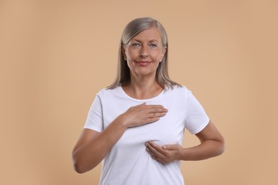 Photo of Beautiful senior woman doing breast self-examination on light brown background