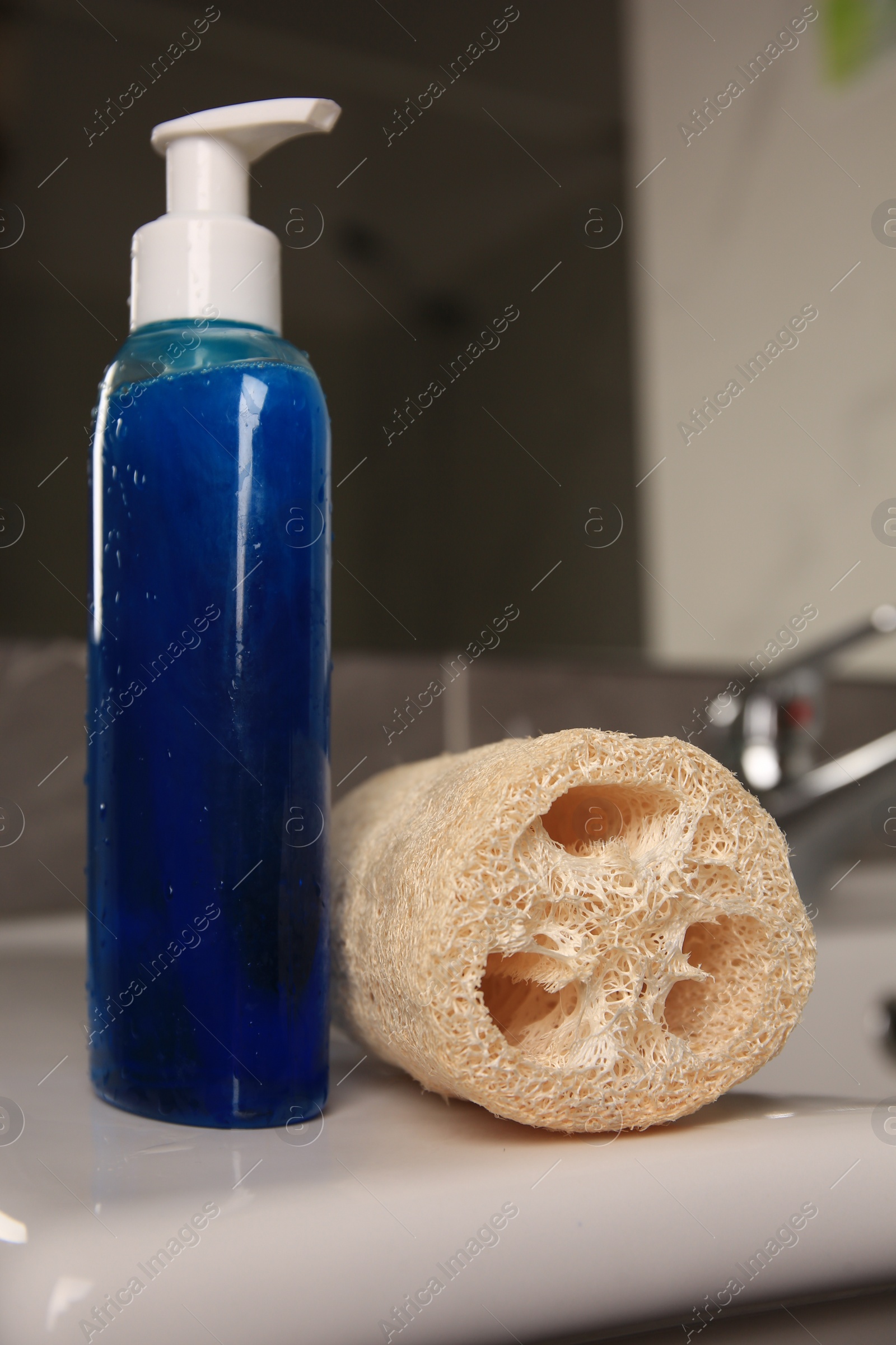 Photo of Natural loofah sponge and bottle with shower gel on washbasin in bathroom