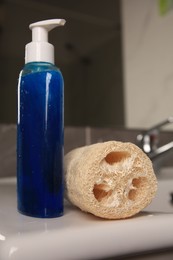 Natural loofah sponge and bottle with shower gel on washbasin in bathroom