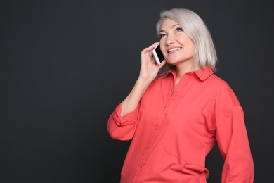 Mature woman talking on mobile phone against black background