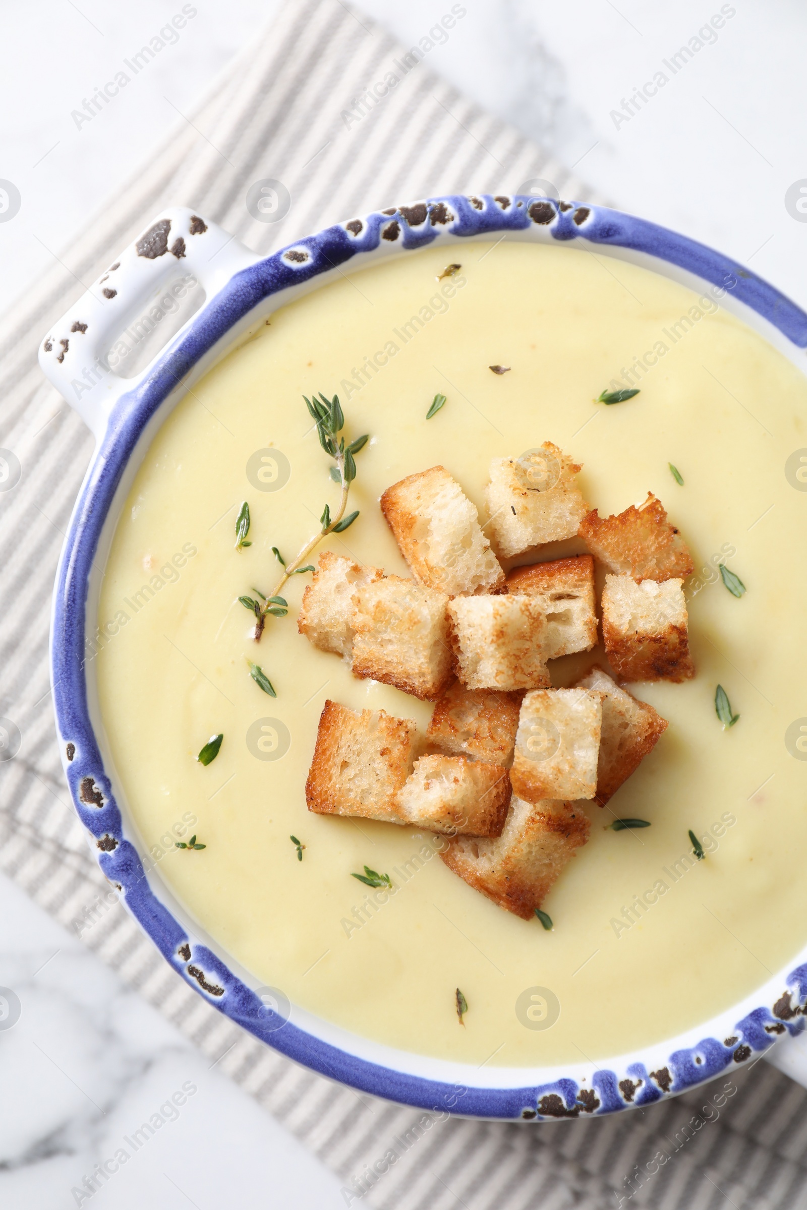 Photo of Tasty potato soup with croutons and rosemary in ceramic pot on white marble table, top view