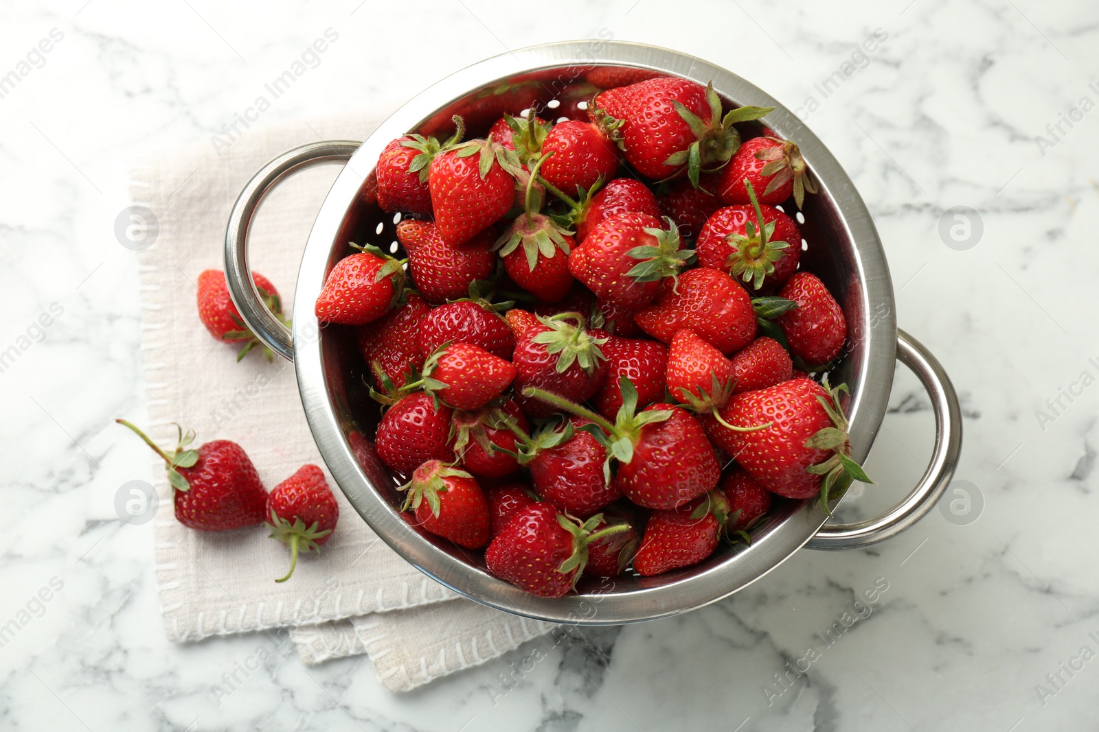 Photo of Metal colander with fresh strawberries on white marble table, top view