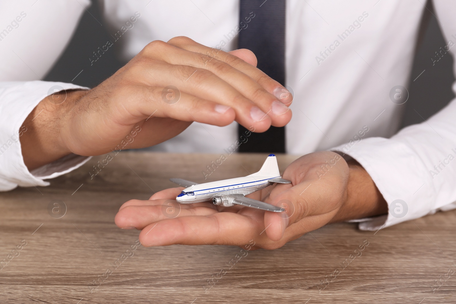 Photo of Insurance agent covering toy plane at table, closeup. Travel safety concept