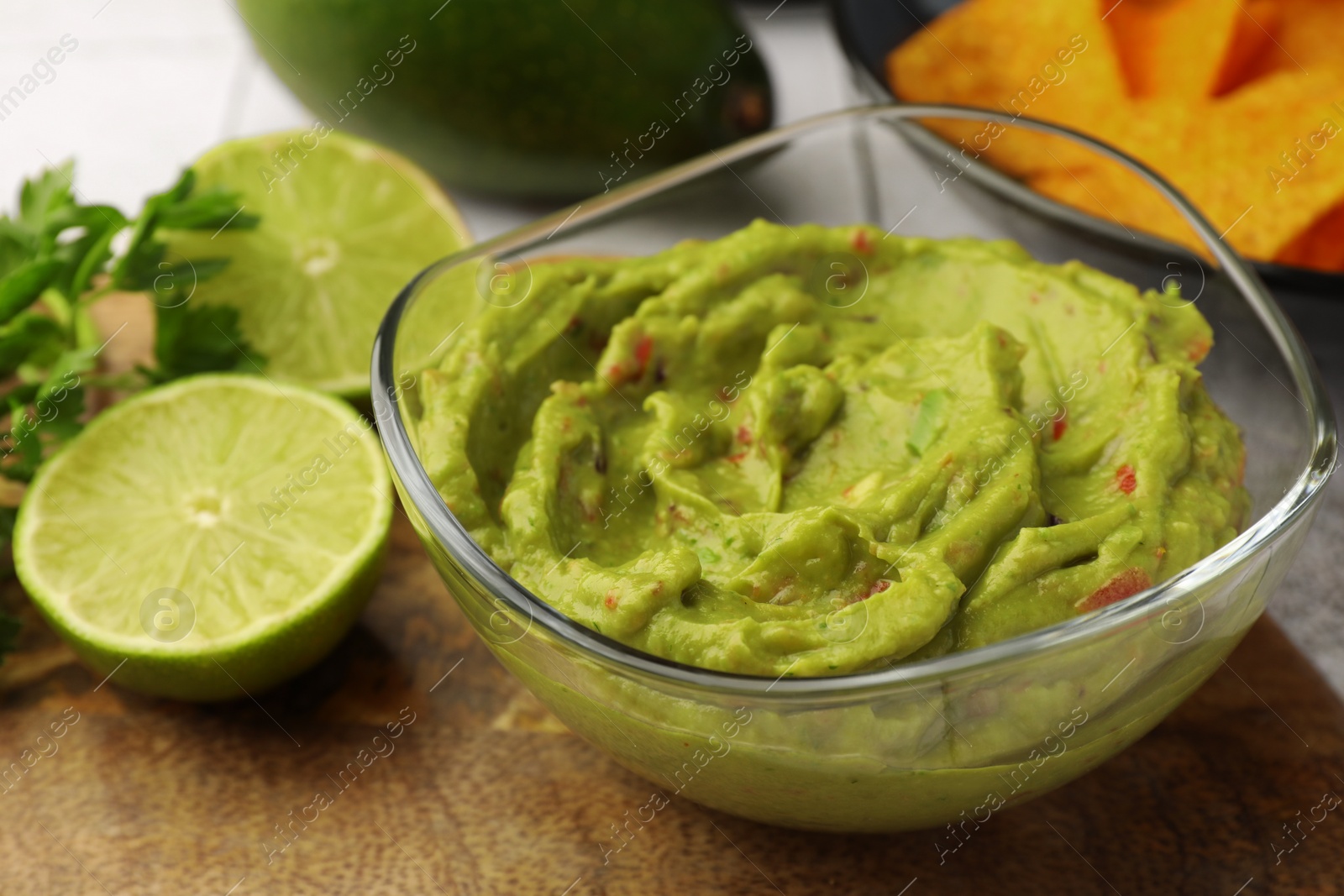 Photo of Bowl of delicious guacamole and lime on wooden board, closeup