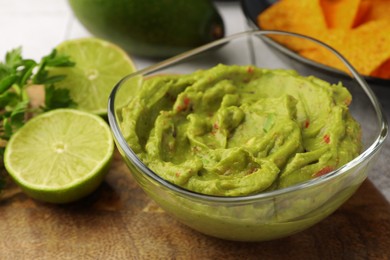 Bowl of delicious guacamole and lime on wooden board, closeup