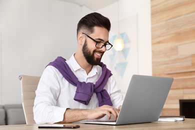 Handsome young man working with laptop at table in home office