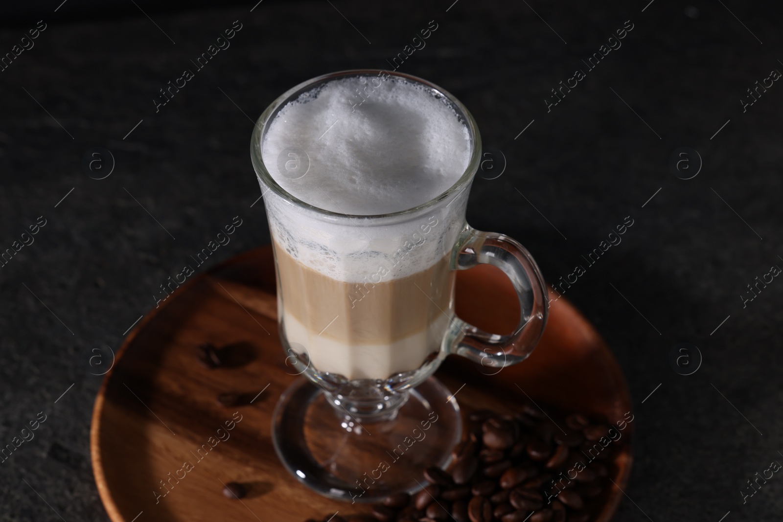 Photo of Aromatic latte macchiato in glass and coffee beans on dark grey table, closeup