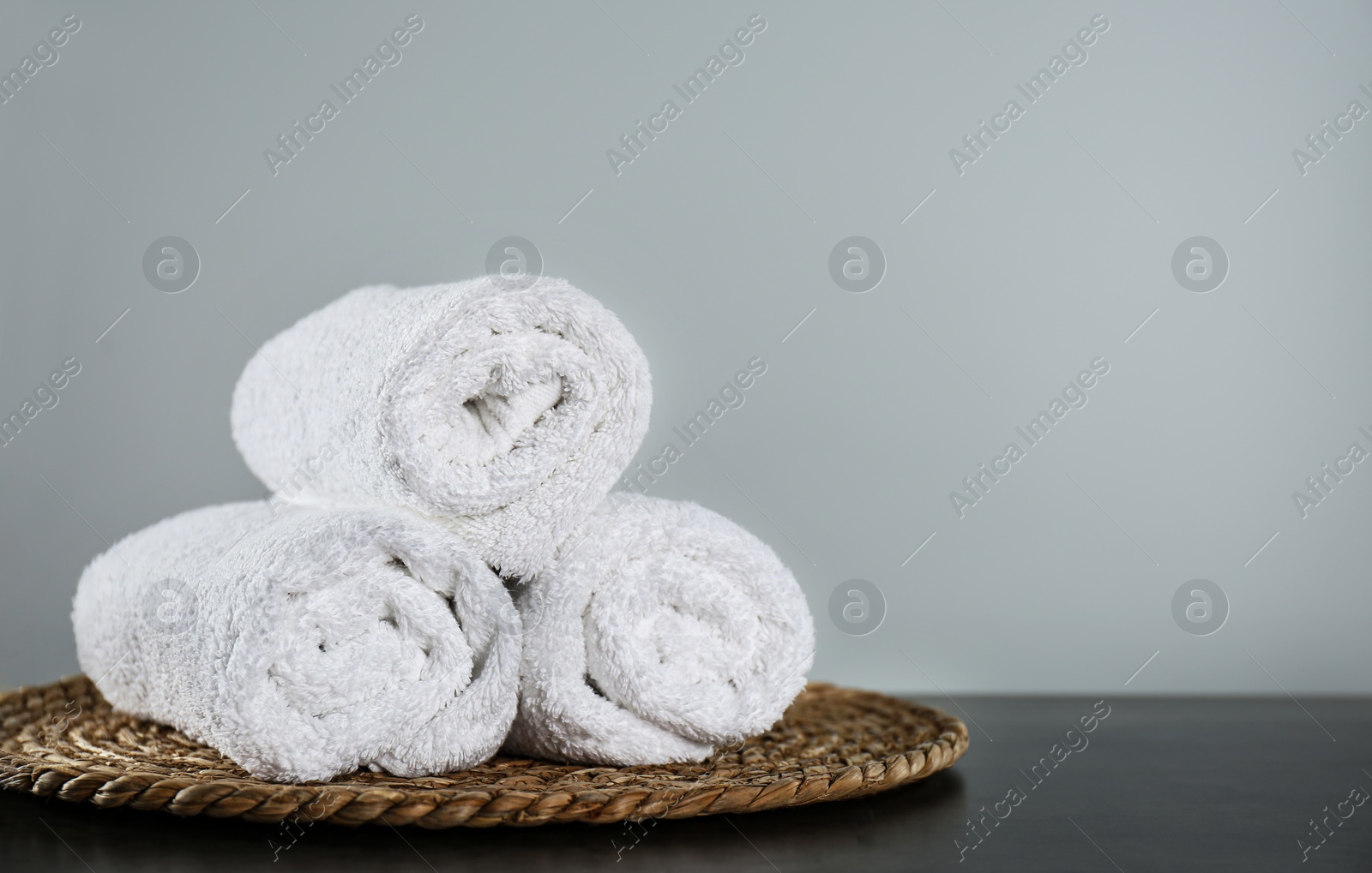 Photo of Clean rolled bath towels and wicker mat on dark grey table. Space for text