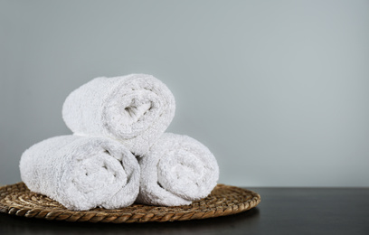 Photo of Clean rolled bath towels and wicker mat on dark grey table. Space for text