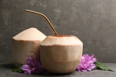 Photo of Young peeled coconuts with straw, palm leaf and beautiful flower on grey table