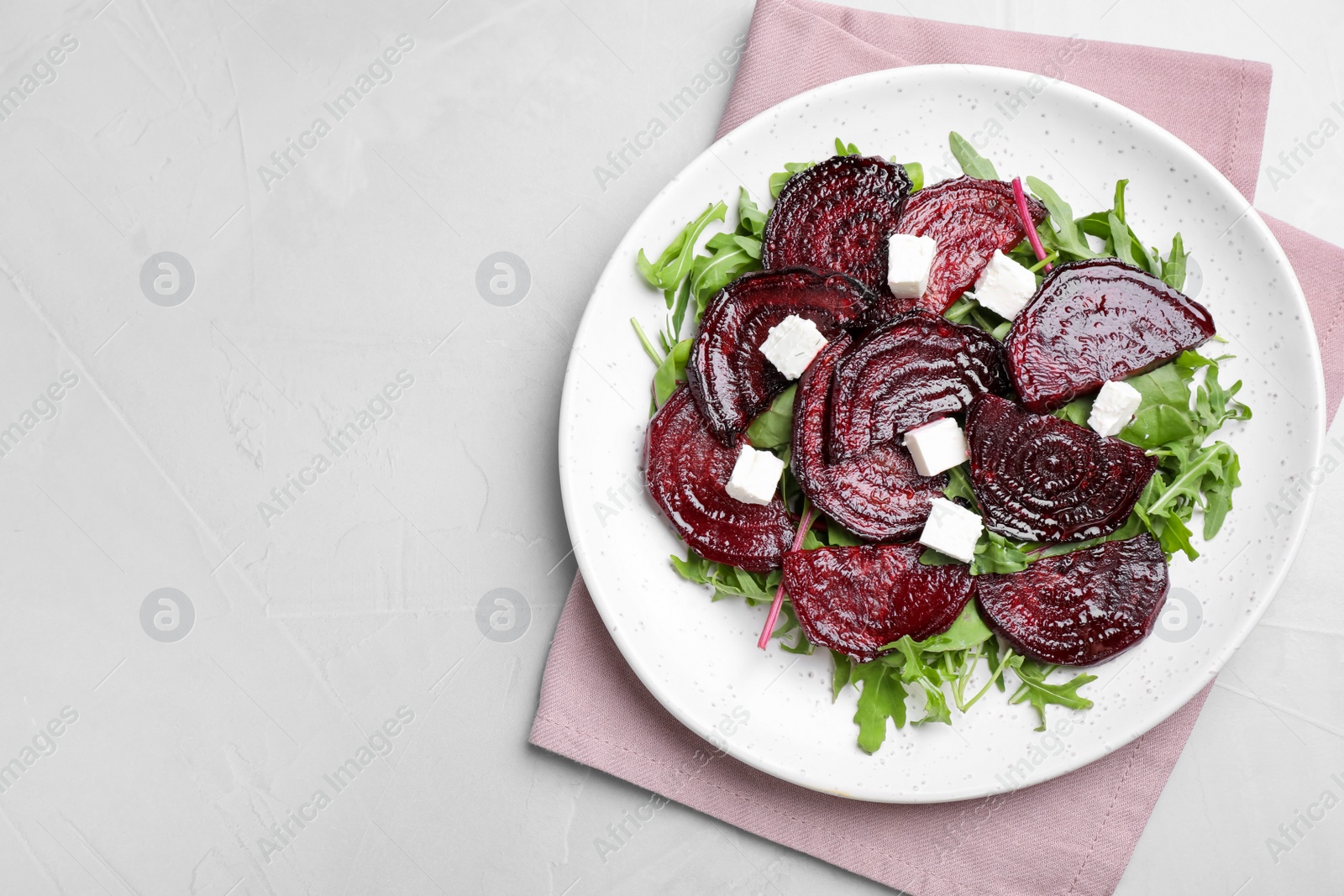 Photo of Roasted beetroot slices with feta cheese and arugula on light grey table, top view. Space for text