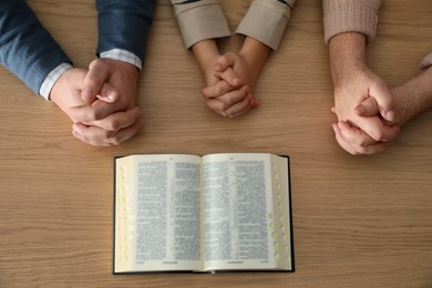 Photo of Boy and his godparents praying together at wooden table, top view