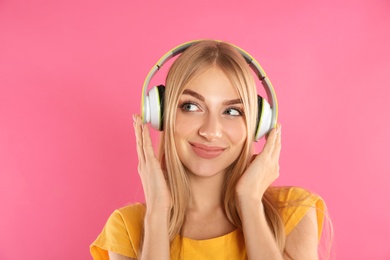 Beautiful young woman listening to music with headphones on color background