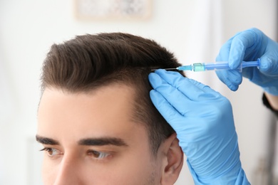 Photo of Young man with hair loss problem receiving injection on blurred background, closeup