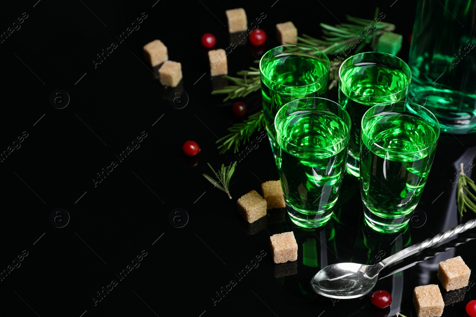 Photo of Absinthe in shot glasses, cranberries, rosemary and brown sugar on mirror table, space for text. Alcoholic drink