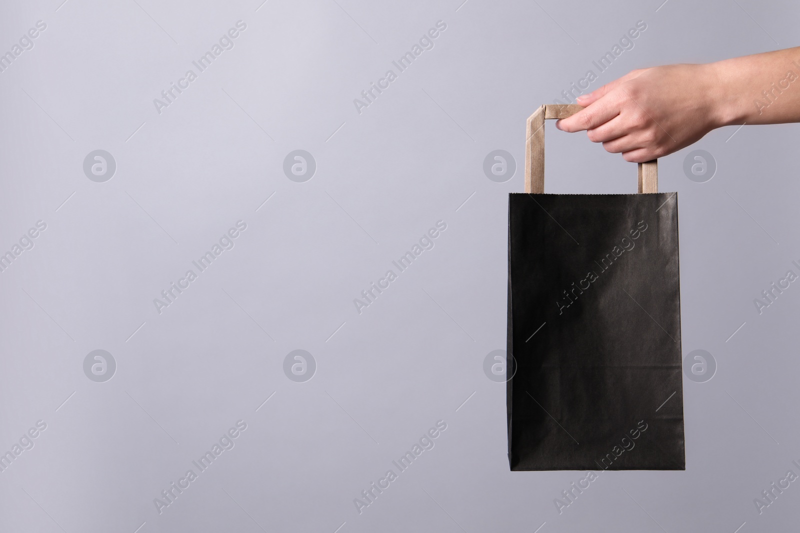 Photo of Woman holding paper shopping bag on grey background, closeup. Space for text