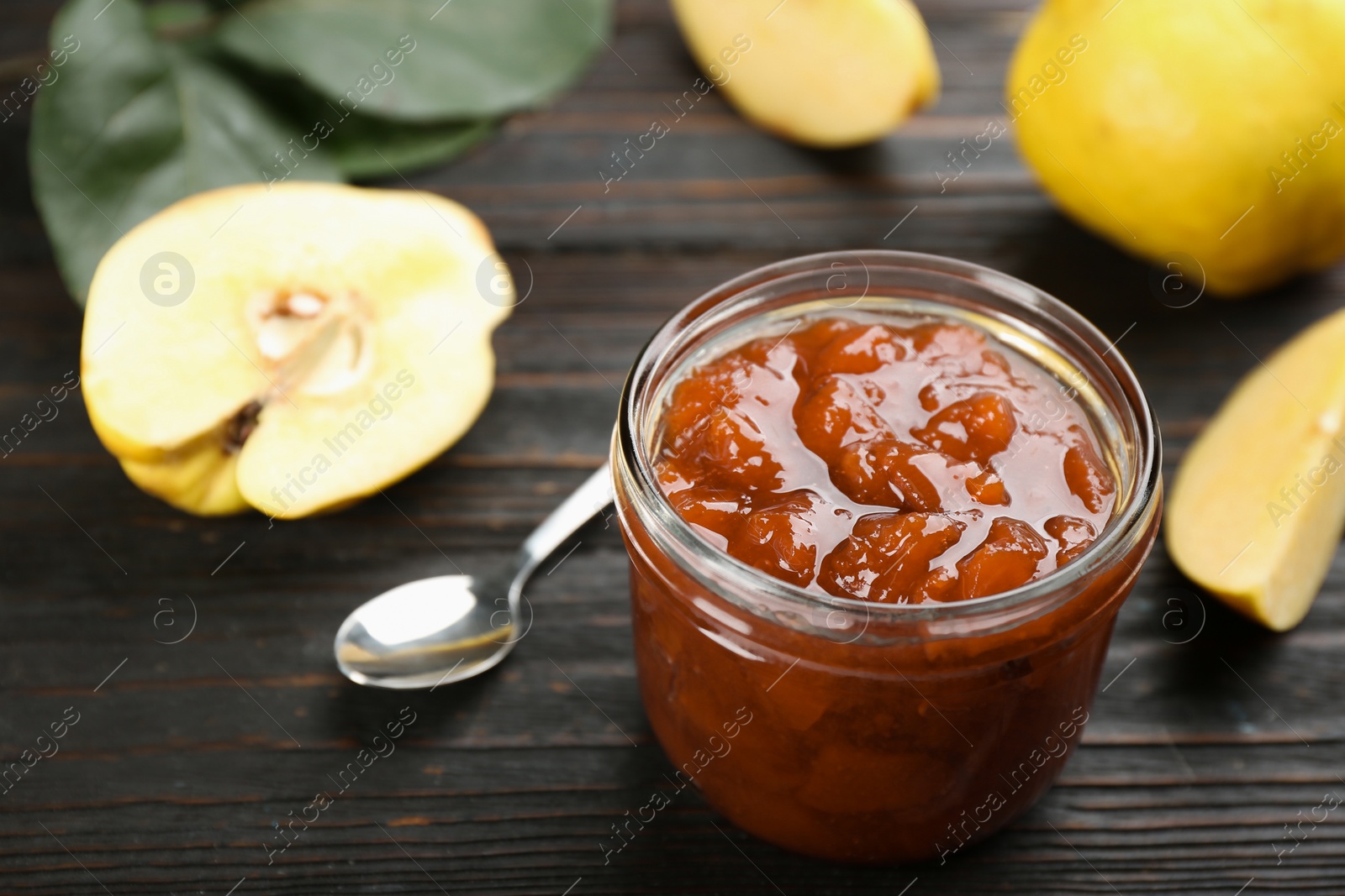 Photo of Delicious quince jam and fruits on black wooden table. Space for text