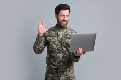 Photo of Happy soldier using video chat on laptop against light grey background. Military service