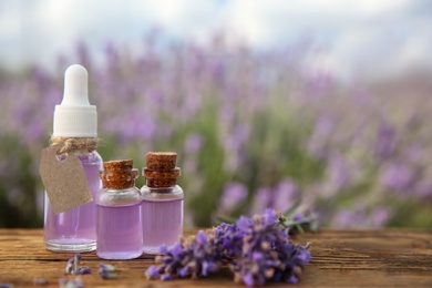 Bottles of natural essential oil and lavender flowers on wooden table, closeup. Space for text