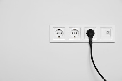 Photo of Power sockets with inserted plug on white wall, space for text. Electrical supply