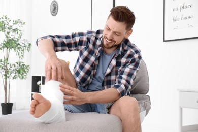 Photo of Mature man with broken leg in cast sitting in armchair at home