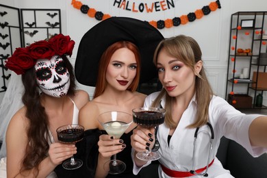 Photo of Group of women in scary costumes with cocktails taking selfie at Halloween party indoors