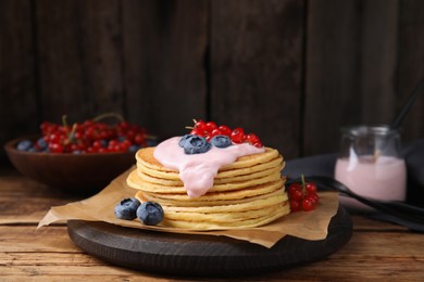 Photo of Tasty pancakes with natural yogurt, blueberries and red currants on wooden table. Space for text